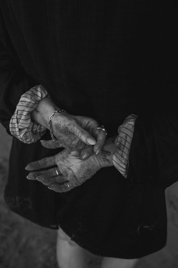A woman's hands, dusted with sand, held loosely behind her back.